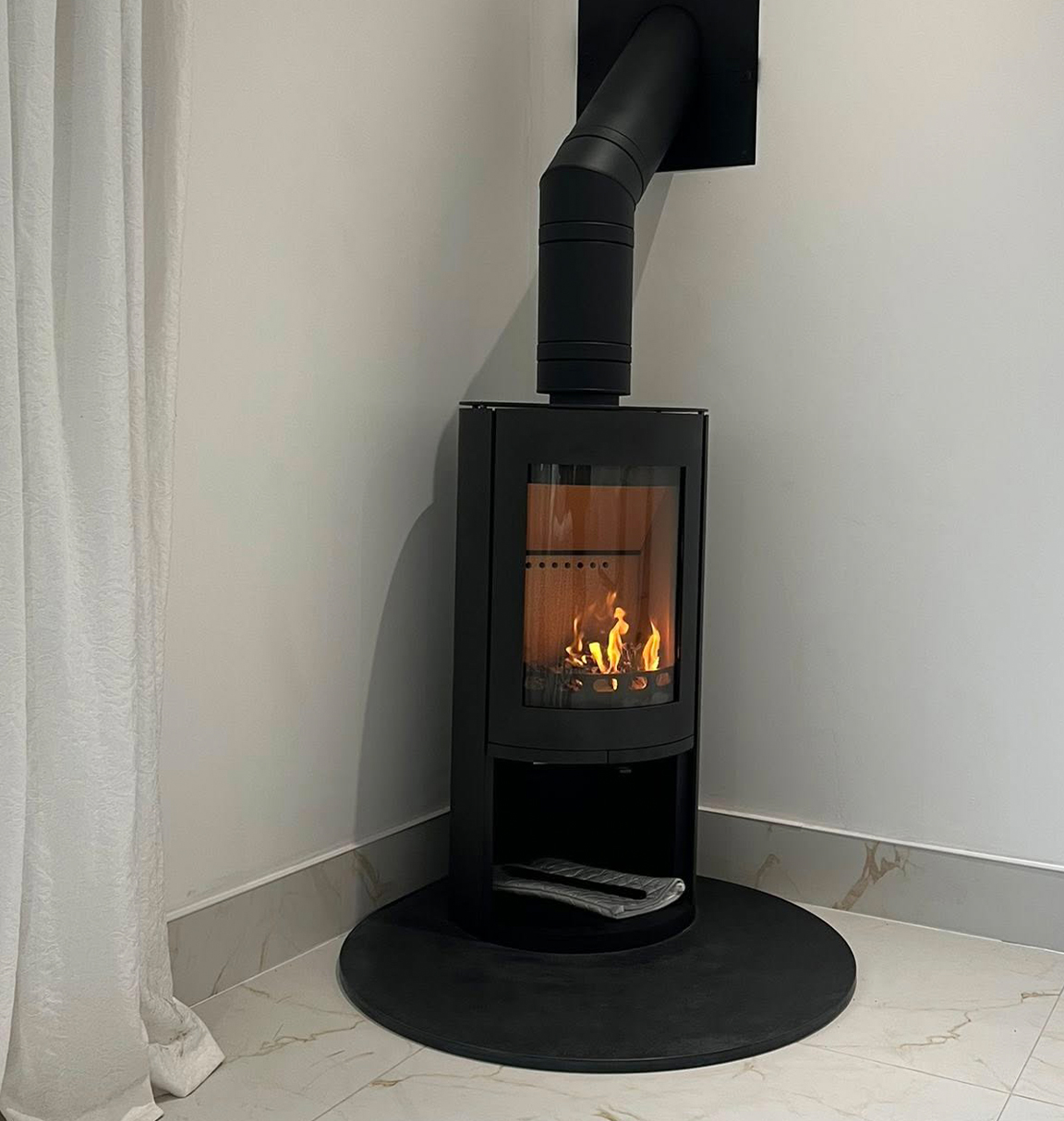 Cylindrical wood burning stove in the corner of a grey room with marble floor